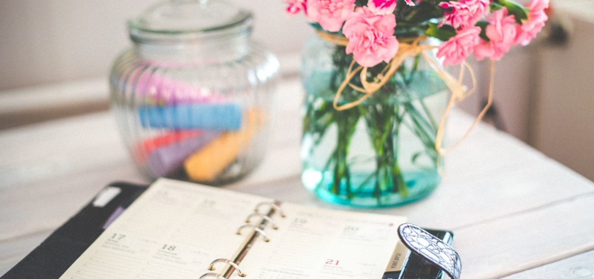 Planner lying open on a desk beside a vase of flowers